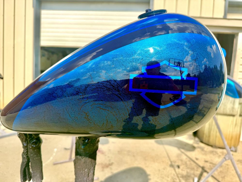 Mirror-blue PVD coated motorcycle tank reflecting the sky and a Harley-Davidson badge outline